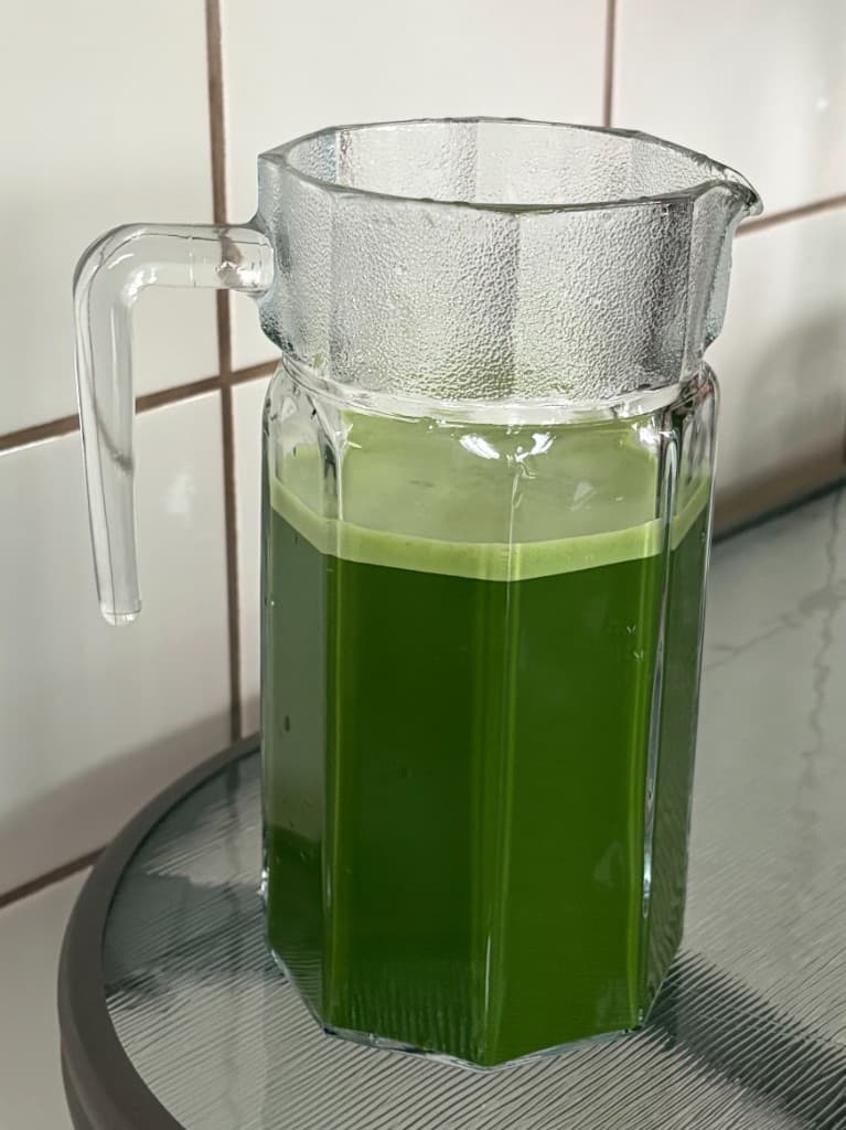 Glass pitcher of vibrant green matcha on a café table
